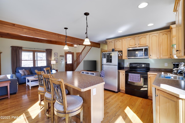 kitchen with light brown cabinetry, a sink, a kitchen breakfast bar, open floor plan, and appliances with stainless steel finishes