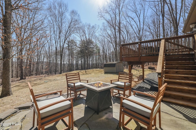 view of patio with an outbuilding, a wooden deck, an outdoor fire pit, stairs, and a storage shed