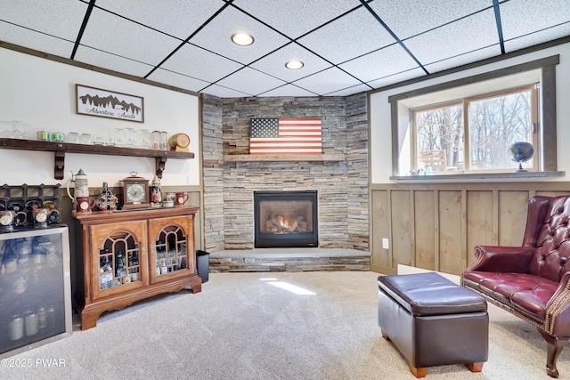 living room featuring carpet flooring, a fireplace, wainscoting, and a paneled ceiling