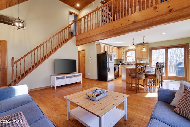 living area with baseboards, stairs, light wood-style floors, and a towering ceiling