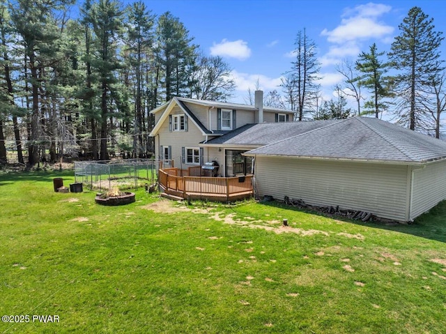 back of property with a wooden deck, fence, roof with shingles, a chimney, and a yard