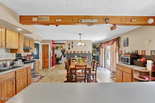 kitchen featuring beamed ceiling, light countertops, under cabinet range hood, a sink, and stainless steel appliances