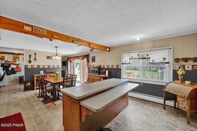 kitchen with a center island, light countertops, a baseboard radiator, stainless steel microwave, and brick patterned floor