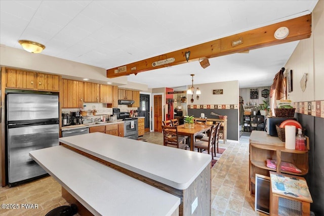 kitchen featuring light countertops, stainless steel appliances, brown cabinets, and under cabinet range hood
