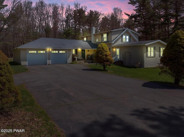 traditional-style house featuring a lawn, an attached garage, a chimney, and aphalt driveway