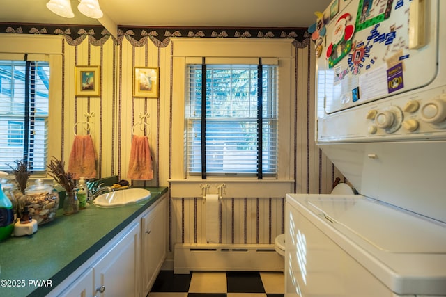 bathroom featuring a healthy amount of sunlight, vanity, stacked washing maching and dryer, and a baseboard radiator