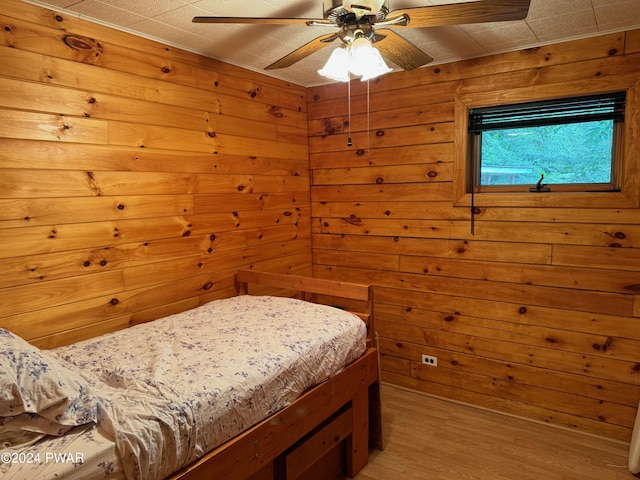 bedroom with hardwood / wood-style flooring, ceiling fan, and wood walls