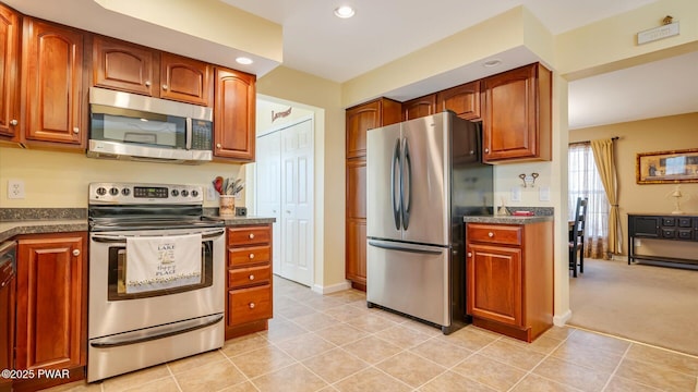 kitchen with recessed lighting, stainless steel appliances, dark countertops, light carpet, and brown cabinetry