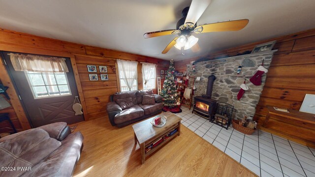 living room featuring light tile patterned floors, a wood stove, a wealth of natural light, and ceiling fan