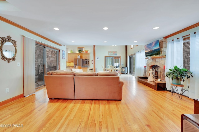 living area with recessed lighting, light wood-style flooring, ornamental molding, a stone fireplace, and baseboards