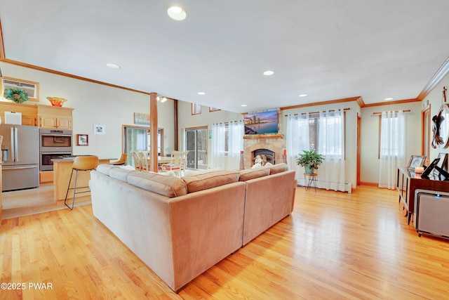 living area with crown molding, light wood finished floors, recessed lighting, a baseboard heating unit, and a stone fireplace