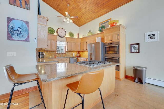 kitchen with appliances with stainless steel finishes, light brown cabinets, light stone counters, and a kitchen breakfast bar