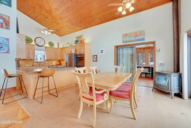 dining area with light tile patterned floors, high vaulted ceiling, wooden ceiling, a ceiling fan, and a wood stove