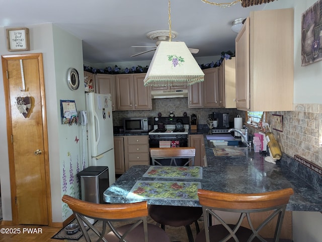 kitchen featuring stainless steel microwave, a sink, backsplash, freestanding refrigerator, and gas range oven