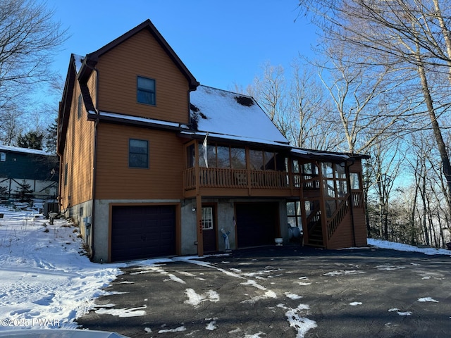 snow covered back of property with a garage and central AC