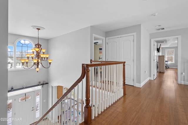 hall featuring plenty of natural light, wood finished floors, an upstairs landing, and an inviting chandelier