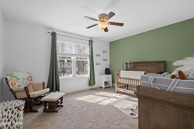 bedroom featuring a crib, ceiling fan, baseboards, and carpet flooring