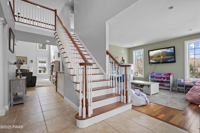 stairs with tile patterned floors, a towering ceiling, and a healthy amount of sunlight