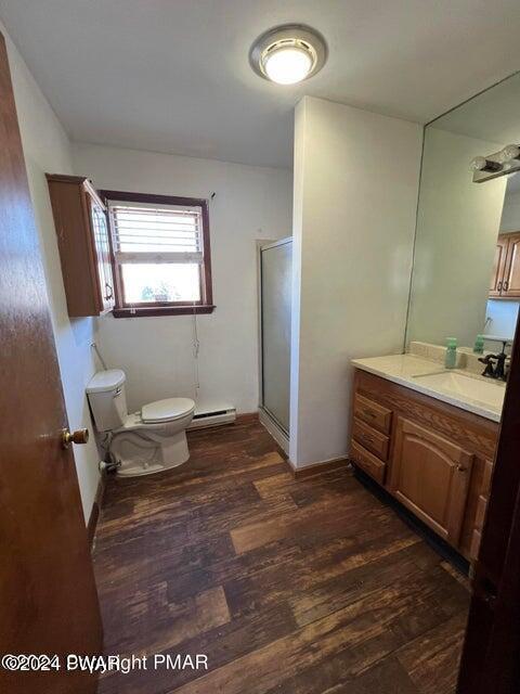 bathroom with hardwood / wood-style floors, vanity, toilet, walk in shower, and a baseboard radiator