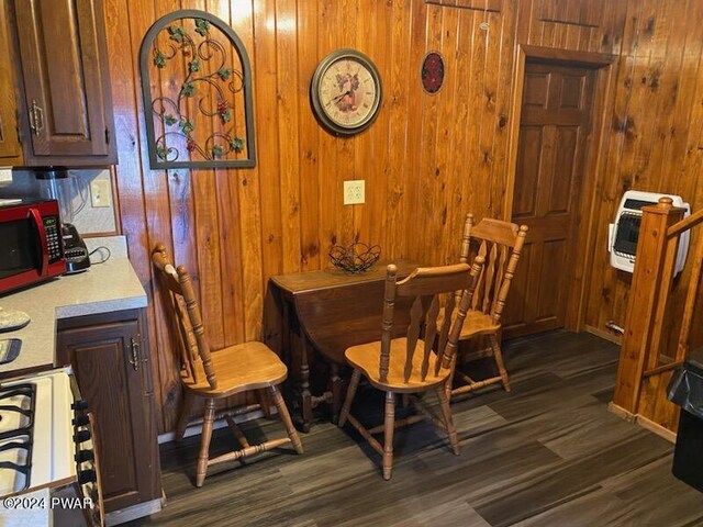 dining room featuring heating unit, dark wood-type flooring, and wood walls