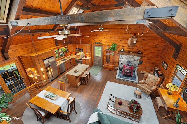 living room featuring beam ceiling, ceiling fan, dark hardwood / wood-style flooring, high vaulted ceiling, and wood walls