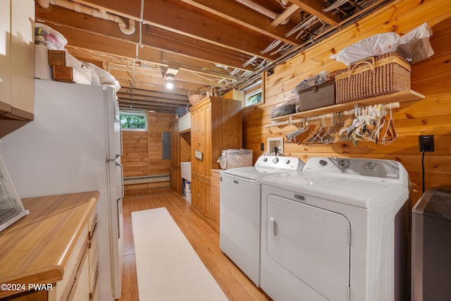 clothes washing area with cabinets, a baseboard heating unit, light hardwood / wood-style flooring, washing machine and dryer, and wood walls