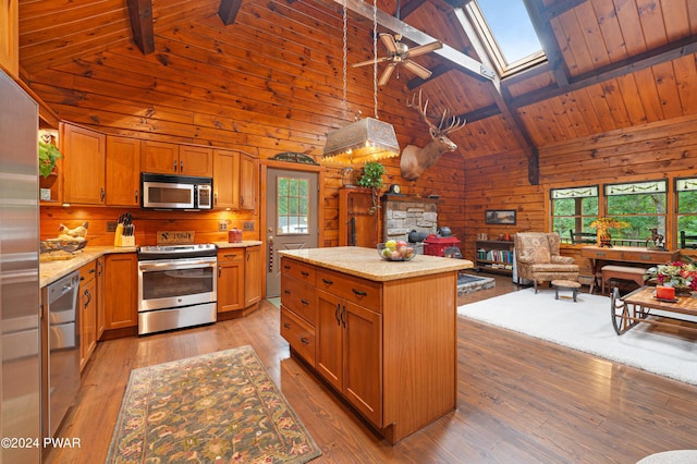 kitchen with beam ceiling, a skylight, stainless steel appliances, light hardwood / wood-style floors, and a kitchen island