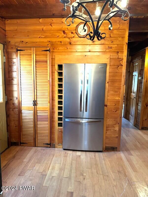 kitchen featuring stainless steel refrigerator, beamed ceiling, wood walls, wood ceiling, and light wood-type flooring