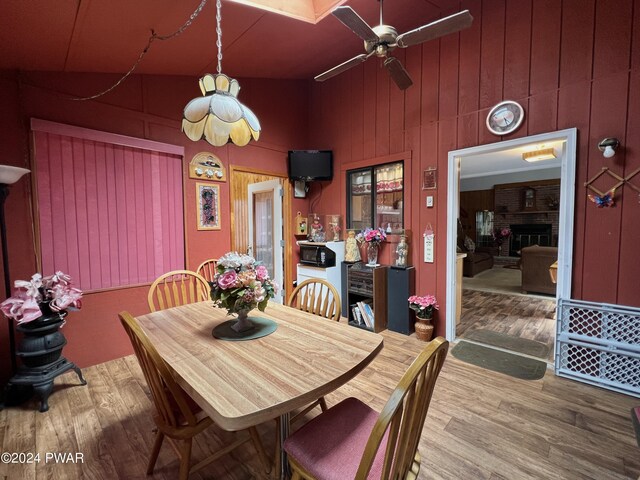 dining area with vaulted ceiling, hardwood / wood-style flooring, a brick fireplace, and ceiling fan