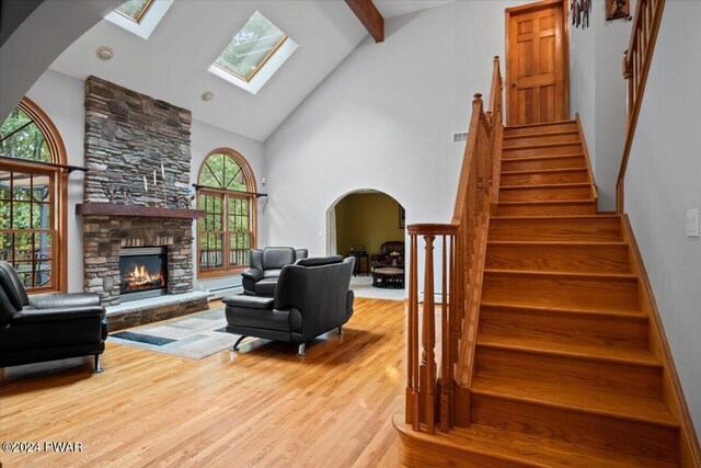 living room with beam ceiling, a skylight, a stone fireplace, light hardwood / wood-style flooring, and high vaulted ceiling