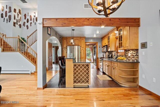 kitchen with a kitchen breakfast bar, light hardwood / wood-style flooring, pendant lighting, decorative backsplash, and appliances with stainless steel finishes