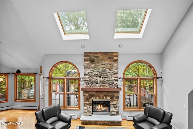 living room featuring baseboard heating, a stone fireplace, and vaulted ceiling with skylight