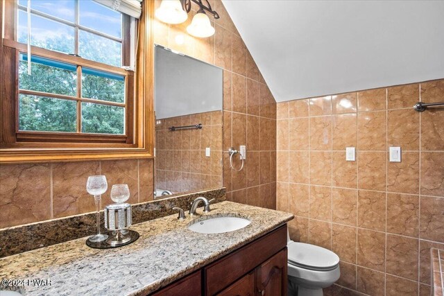 bathroom with vanity, plenty of natural light, tile walls, and lofted ceiling