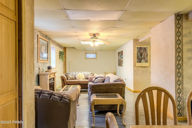 living area with a ceiling fan, a paneled ceiling, baseboards, and wood finished floors