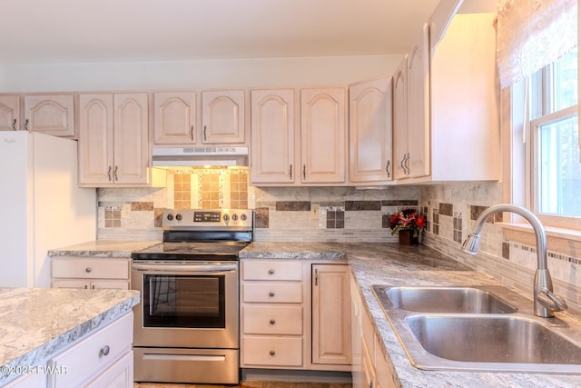 kitchen with under cabinet range hood, a sink, light countertops, stainless steel electric range, and freestanding refrigerator