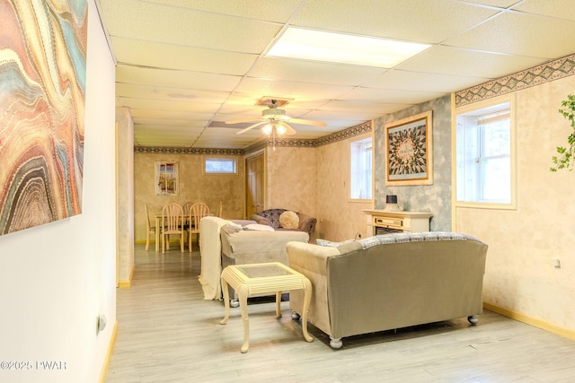 living area featuring light wood-style floors, ceiling fan, baseboards, and a drop ceiling