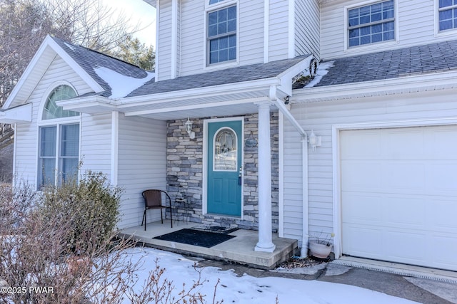 doorway to property featuring a garage, stone siding, and roof with shingles