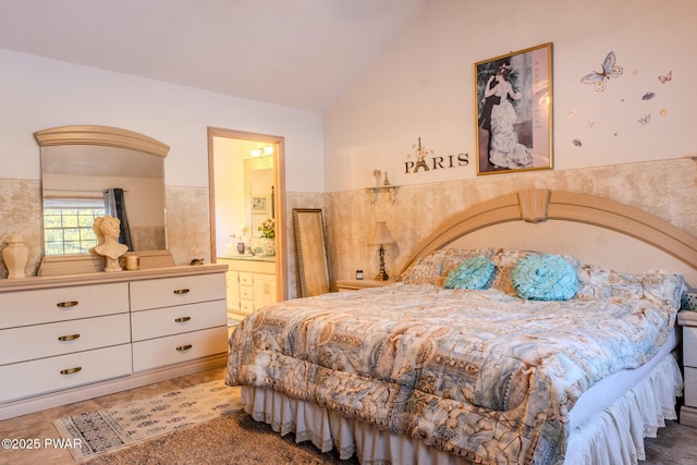 bedroom featuring vaulted ceiling, wainscoting, and ensuite bath