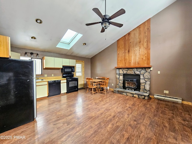 kitchen with ceiling fan, baseboard heating, black appliances, a stone fireplace, and light wood-type flooring