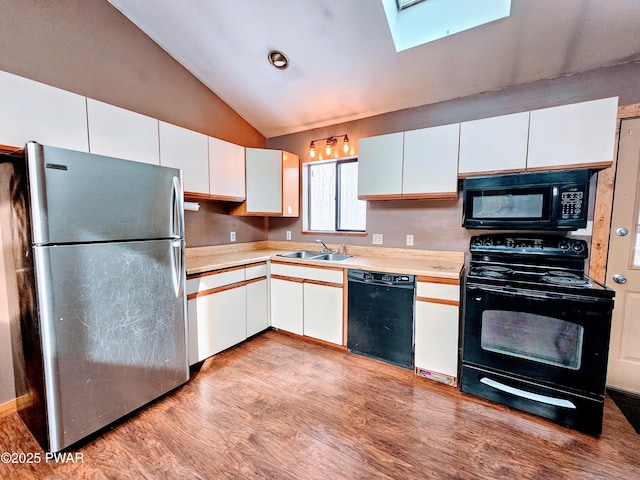 kitchen with lofted ceiling with skylight, sink, black appliances, light wood-type flooring, and white cabinets