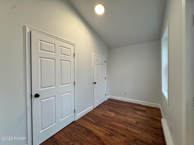 unfurnished bedroom with lofted ceiling, dark wood-type flooring, baseboard heating, and baseboards
