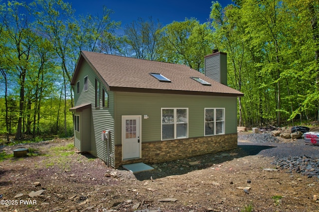 view of side of property with a chimney, a shingled roof, and stone siding