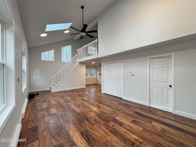 unfurnished living room featuring high vaulted ceiling, dark wood finished floors, a ceiling fan, stairs, and a skylight