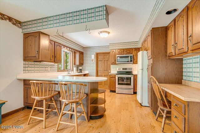 146 Cove Point Cir, Lakeville, PA 18438 - kitchen featuring stainless steel appliances, a peninsula, wallpapered walls, brown cabinetry, and a textured ceiling