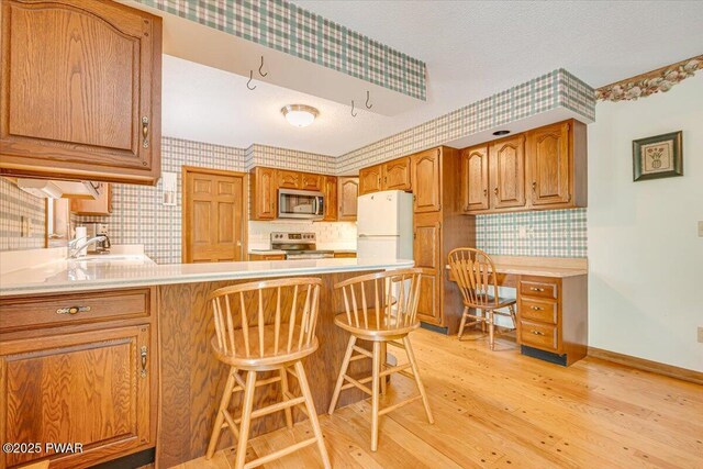 146 Cove Point Cir, Lakeville, PA 18438 - kitchen with stainless steel appliances, wallpapered walls, light wood-style floors, a peninsula, and brown cabinets
