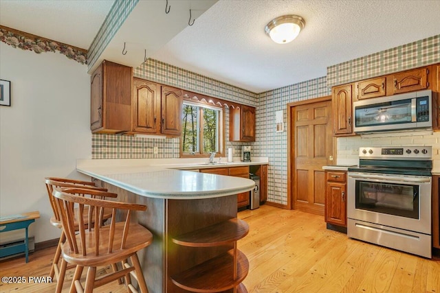 146 Cove Point Cir, Lakeville, PA 18438 - kitchen with appliances with stainless steel finishes, wallpapered walls, a sink, light wood finished floors, and a peninsula