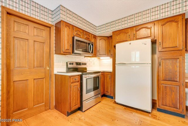 146 Cove Point Cir, Lakeville, PA 18438 - kitchen featuring wallpapered walls, appliances with stainless steel finishes, light wood-style floors, brown cabinetry, and light countertops