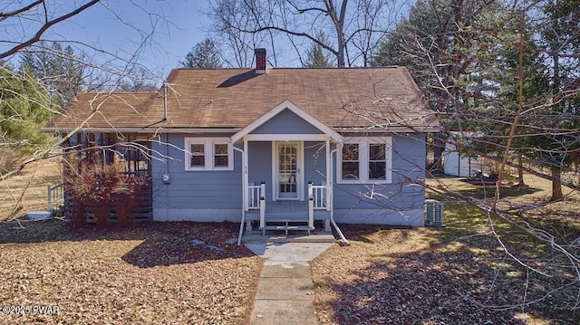 view of front of property with cooling unit, roof with shingles, and a chimney