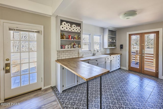 kitchen featuring open shelves, a sink, tasteful backsplash, french doors, and butcher block counters