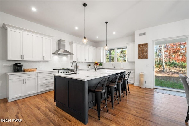 kitchen featuring decorative light fixtures, white cabinetry, wall chimney exhaust hood, and a center island with sink